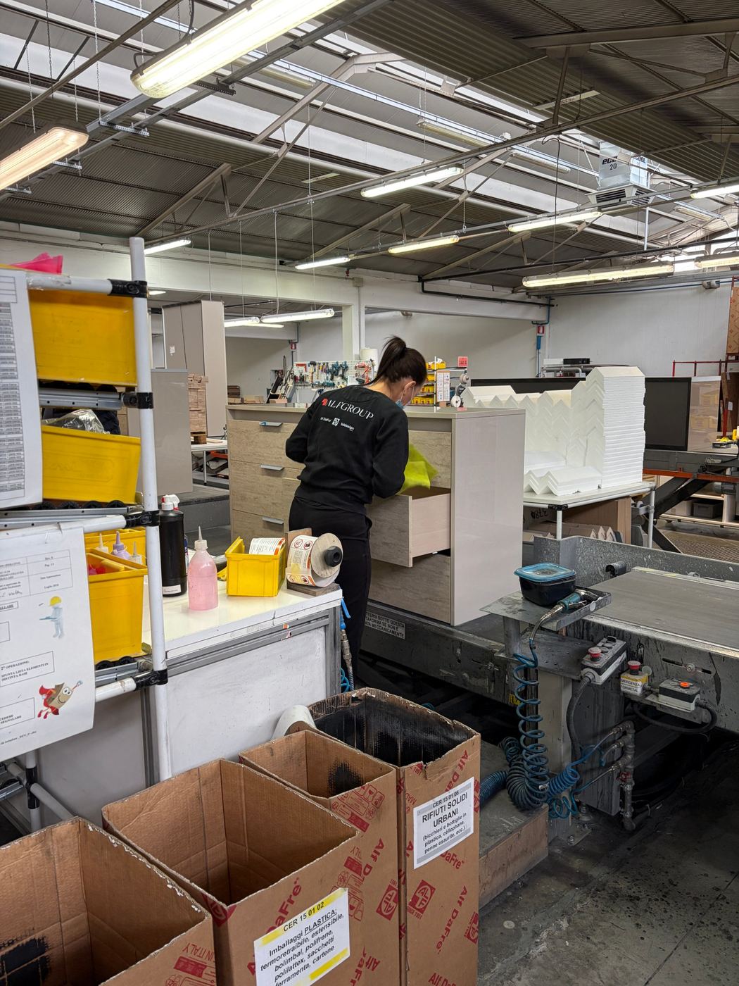 A final check of a chest of drawers at a factory packing station, with sorted recycling bins in the foreground