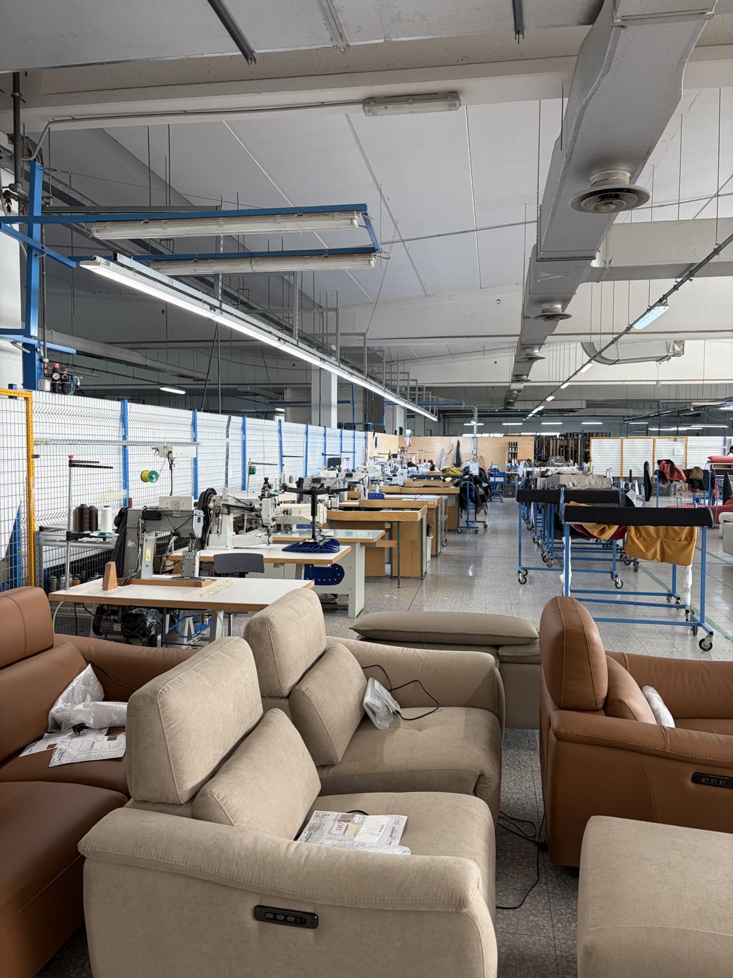 A sewing line in an Italian upholstery workshop, with finished leather recliners in the foreground